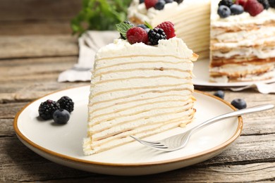 Photo of Piece of tasty crepe cake with berries served on wooden table, closeup