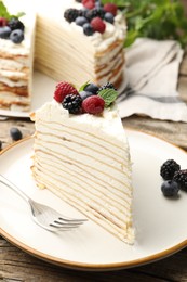 Photo of Piece of tasty crepe cake with berries served on wooden table, closeup