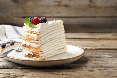 Photo of Piece of tasty crepe cake with berries served on wooden table, closeup. Space for text