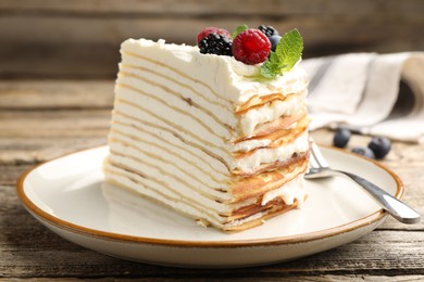 Photo of Piece of tasty crepe cake with berries served on wooden table, closeup