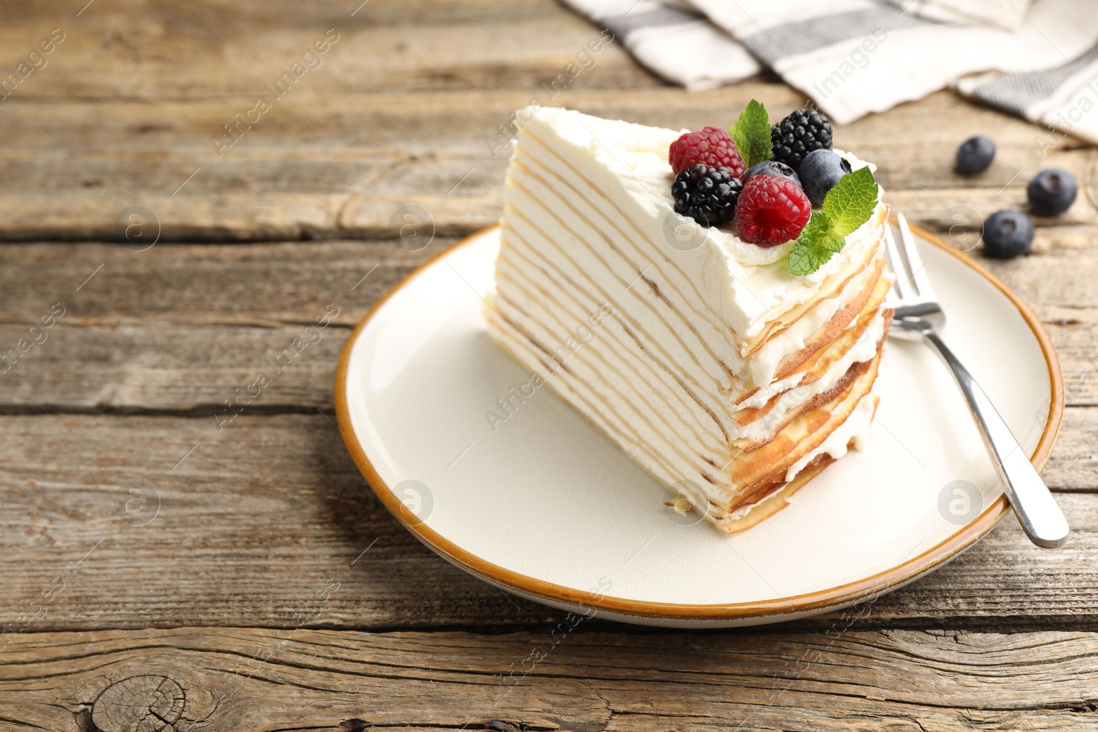 Photo of Piece of tasty crepe cake with berries served on wooden table, closeup. Space for text