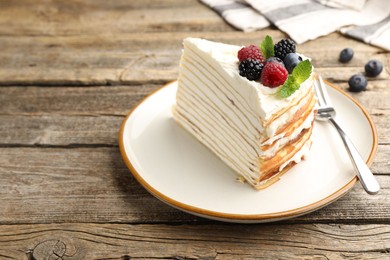 Photo of Piece of tasty crepe cake with berries served on wooden table, closeup. Space for text