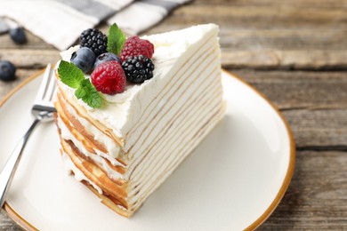 Photo of Piece of tasty crepe cake with berries served on wooden table, closeup