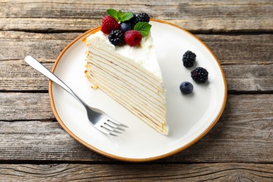 Photo of Piece of tasty crepe cake with berries served on wooden table, closeup
