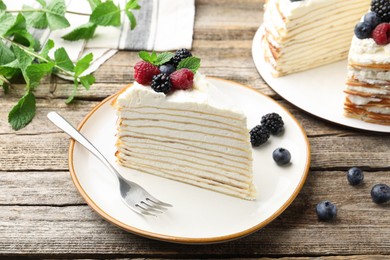 Photo of Piece of tasty crepe cake with berries served on wooden table, closeup