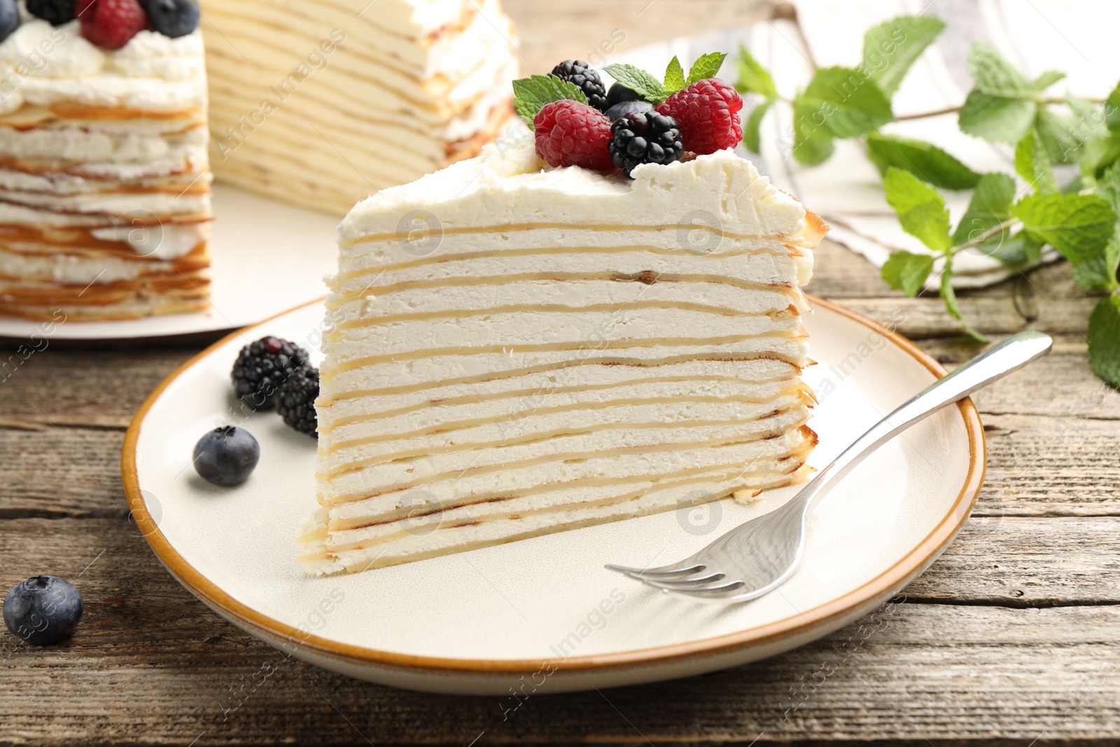 Photo of Piece of tasty crepe cake with berries served on wooden table, closeup