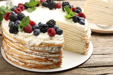 Photo of Tasty crepe cake with berries and mint on wooden table, closeup