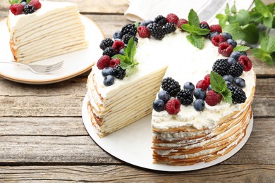 Photo of Tasty crepe cake with berries and mint on wooden table