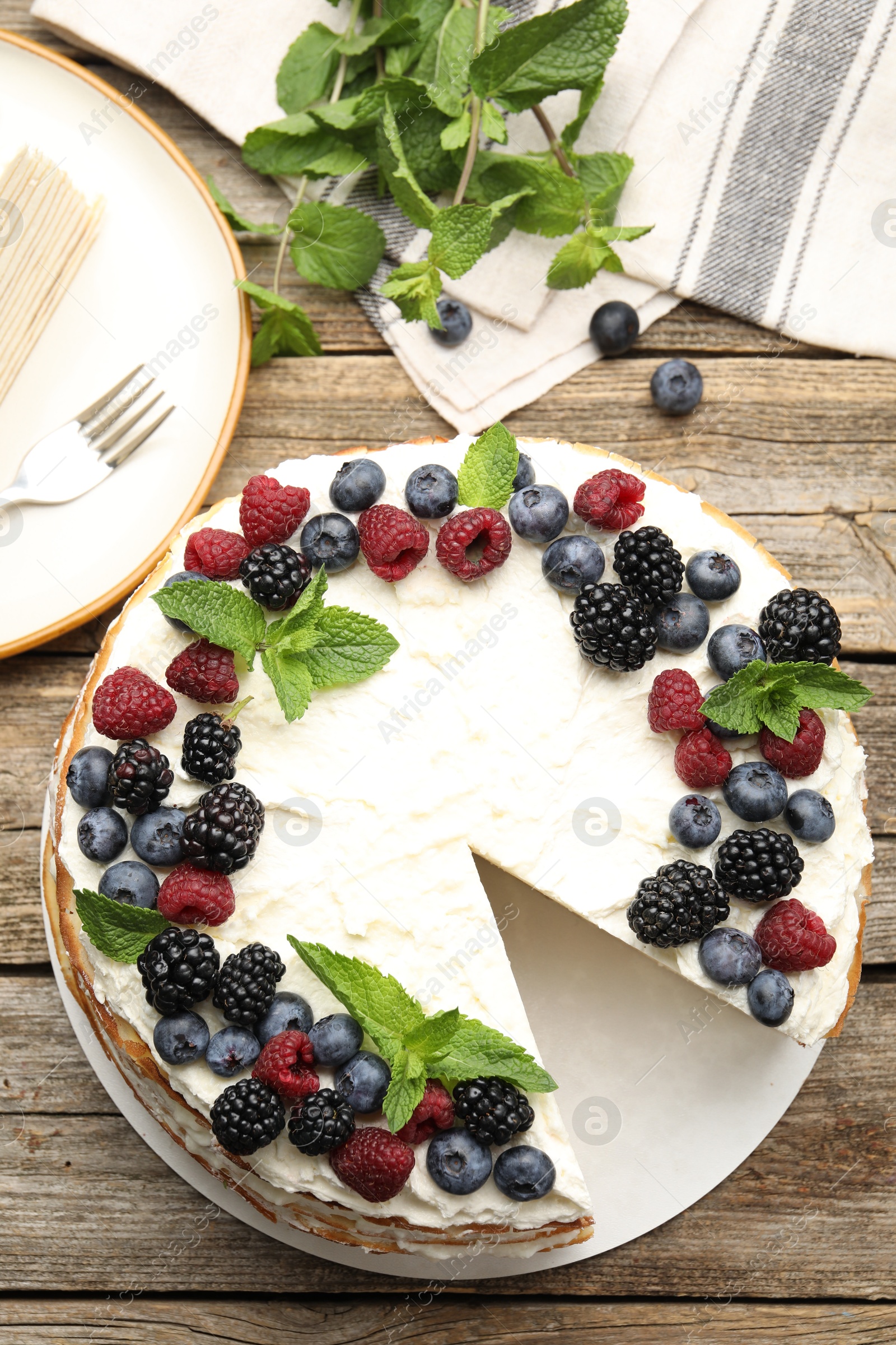 Photo of Tasty crepe cake with berries on wooden table, flat lay