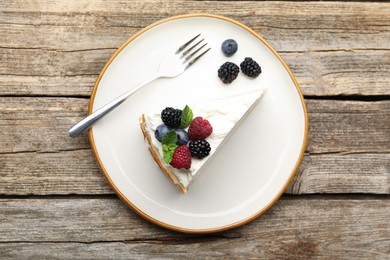 Photo of Piece of tasty crepe cake with berries served on wooden table, top view