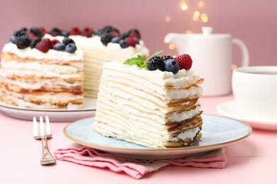Photo of Piece of tasty crepe cake with berries served on pink wooden table against blurred lights, closeup