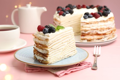 Photo of Piece of tasty crepe cake with berries served on pink wooden table against blurred lights, closeup