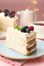 Photo of Piece of tasty crepe cake with berries served on pink wooden table against blurred lights, closeup
