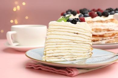 Photo of Piece of tasty crepe cake with berries served on pink wooden table against blurred lights, closeup
