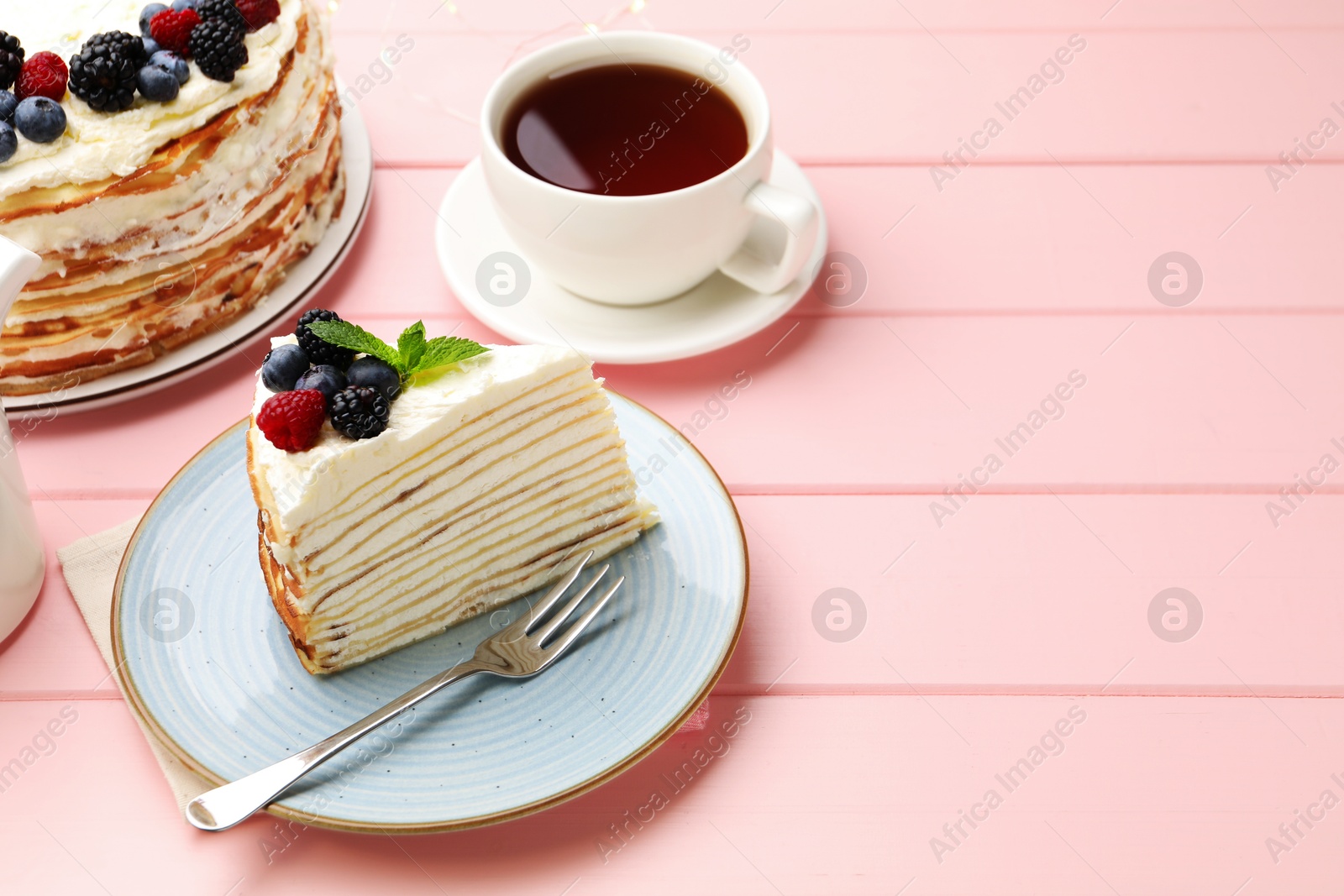 Photo of Piece of tasty crepe cake with berries served on pink wooden table, closeup. Space for text