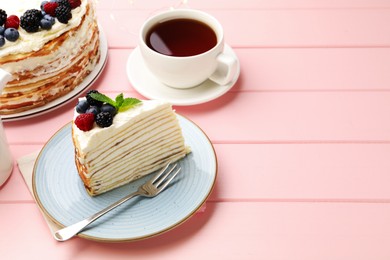 Photo of Piece of tasty crepe cake with berries served on pink wooden table, closeup. Space for text