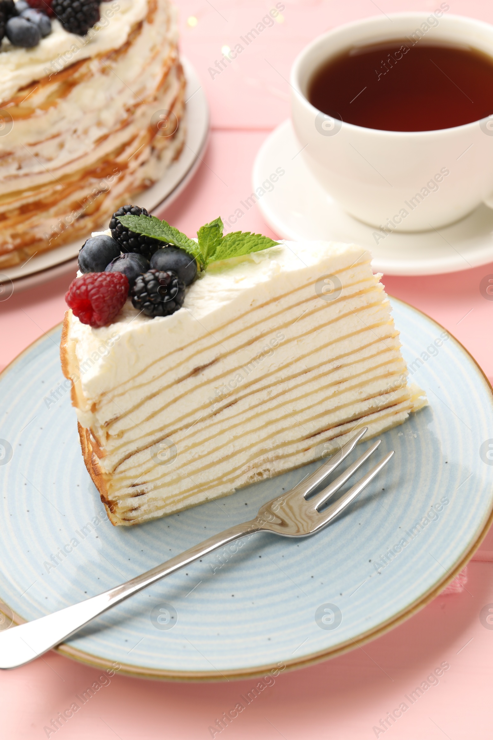 Photo of Piece of tasty crepe cake with berries served on pink wooden table, closeup