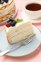 Photo of Piece of tasty crepe cake with berries served on pink wooden table, closeup