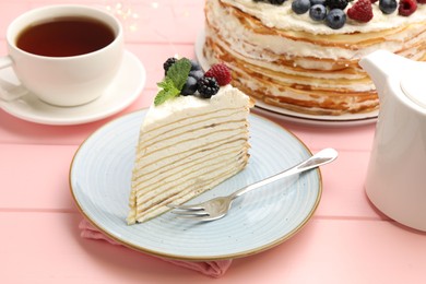 Photo of Piece of tasty crepe cake with berries served on pink wooden table, closeup
