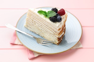 Photo of Piece of tasty crepe cake with berries served on pink wooden table, closeup