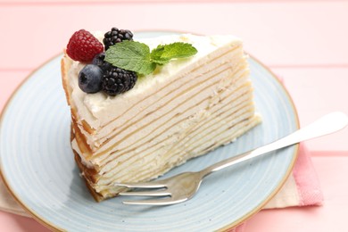 Photo of Piece of tasty crepe cake with berries served on pink wooden table, closeup