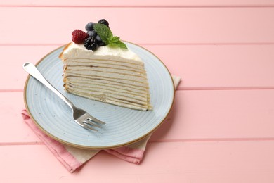 Photo of Piece of tasty crepe cake with berries served on pink wooden table, closeup. Space for text