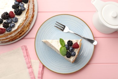 Photo of Piece of tasty crepe cake with berries served on pink wooden table, flat lay