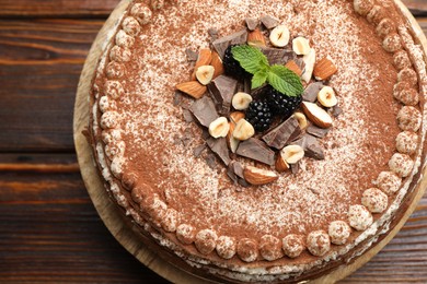 Photo of Delicious crepe cake with chocolate, nuts, blackberries and cocoa powder on wooden table, top view