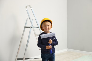 Photo of Choice of profession. Little boy with paint roller pretending to be painter indoors