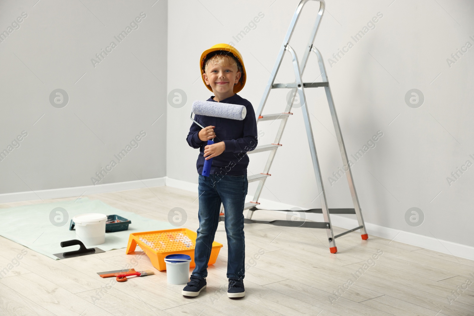 Photo of Choice of profession. Little boy with paint roller pretending to be painter indoors