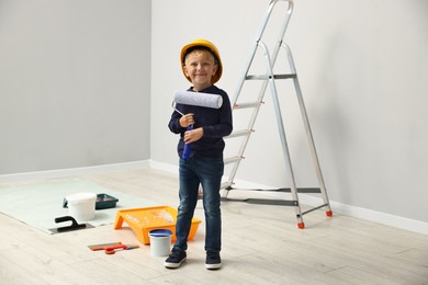 Photo of Choice of profession. Little boy with paint roller pretending to be painter indoors