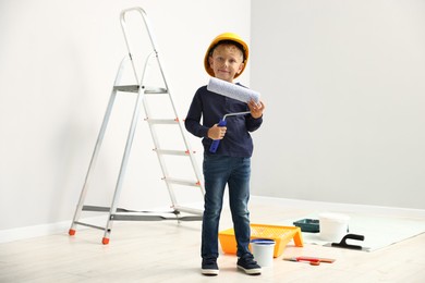 Photo of Choice of profession. Little boy with paint roller pretending to be painter indoors
