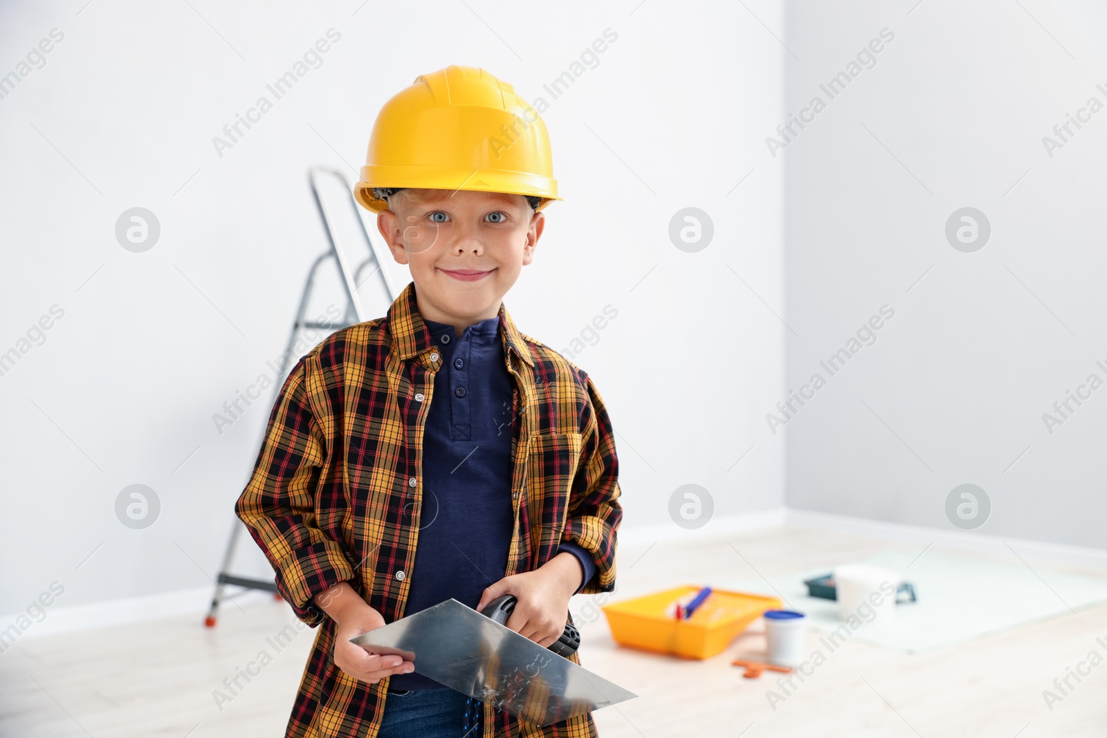 Photo of Choice of profession. Little boy with spatula tool pretending to be builder indoors. Space for text
