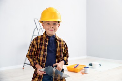Photo of Choice of profession. Little boy with spatula tool pretending to be builder indoors. Space for text