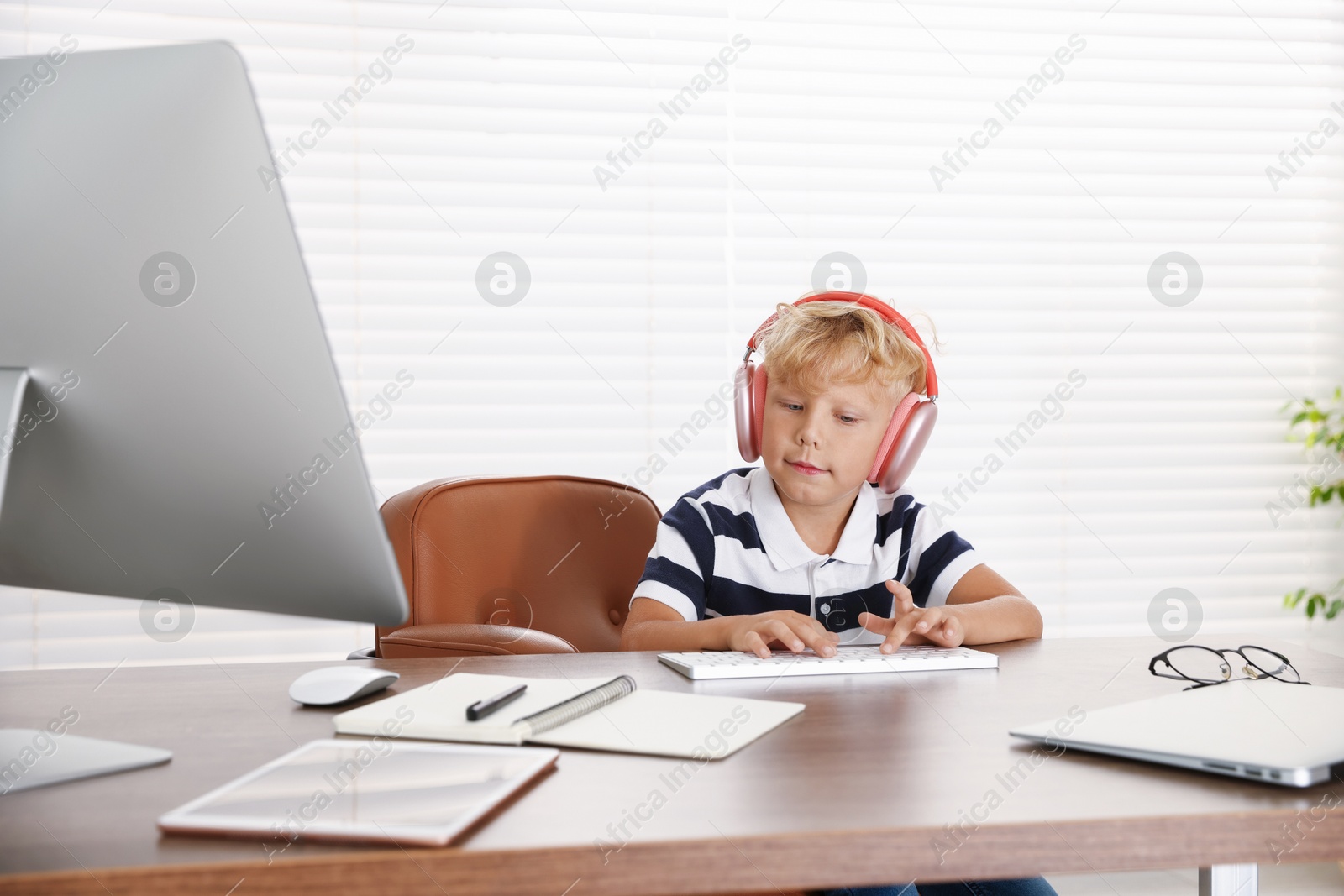 Photo of Choice of profession. Little boy with headphones pretending to work on computer in office