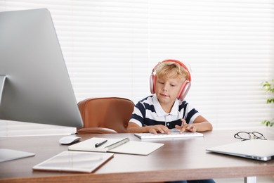 Photo of Choice of profession. Little boy with headphones pretending to work on computer in office