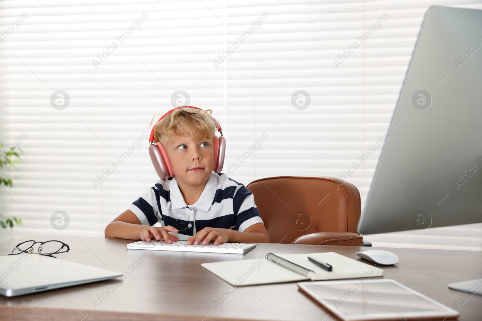 Photo of Choice of profession. Little boy with headphones pretending to work on computer in office