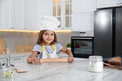 Photo of Choice of profession. Little girl with rolling pin pretending to be chef in kitchen