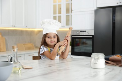 Photo of Choice of profession. Little girl with rolling pin pretending to be chef in kitchen