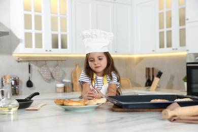 Photo of Choice of profession. Little girl with pastries pretending to be chef in kitchen