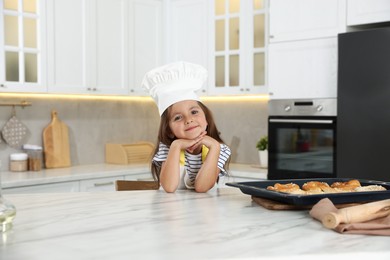 Photo of Choice of profession. Little girl with pastries pretending to be chef in kitchen