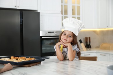 Photo of Choice of profession. Little girl with pastries pretending to be chef in kitchen