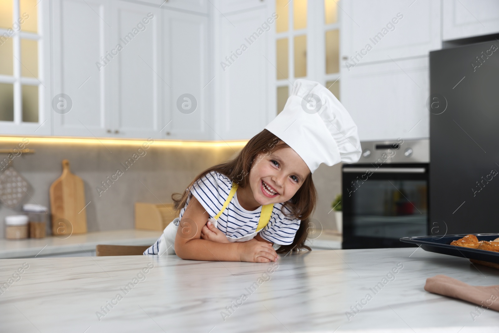 Photo of Choice of profession. Little girl pretending to be chef at table in kitchen