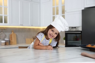 Photo of Choice of profession. Little girl pretending to be chef at table in kitchen