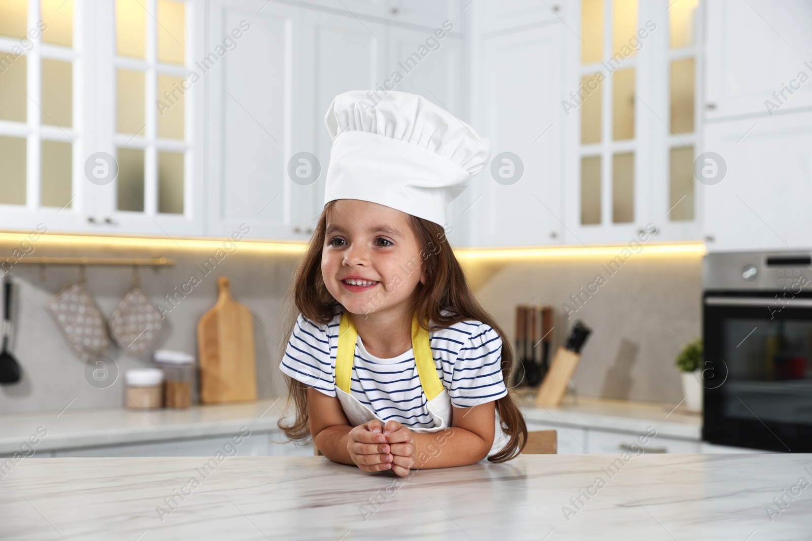 Photo of Choice of profession. Little girl pretending to be chef at table in kitchen