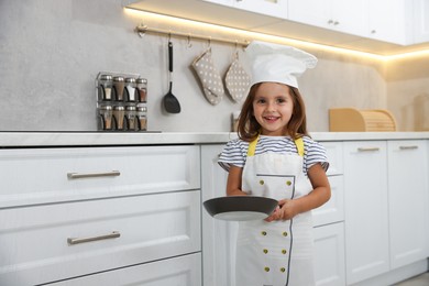 Photo of Choice of profession. Little girl with frying pan pretending to be chef in kitchen