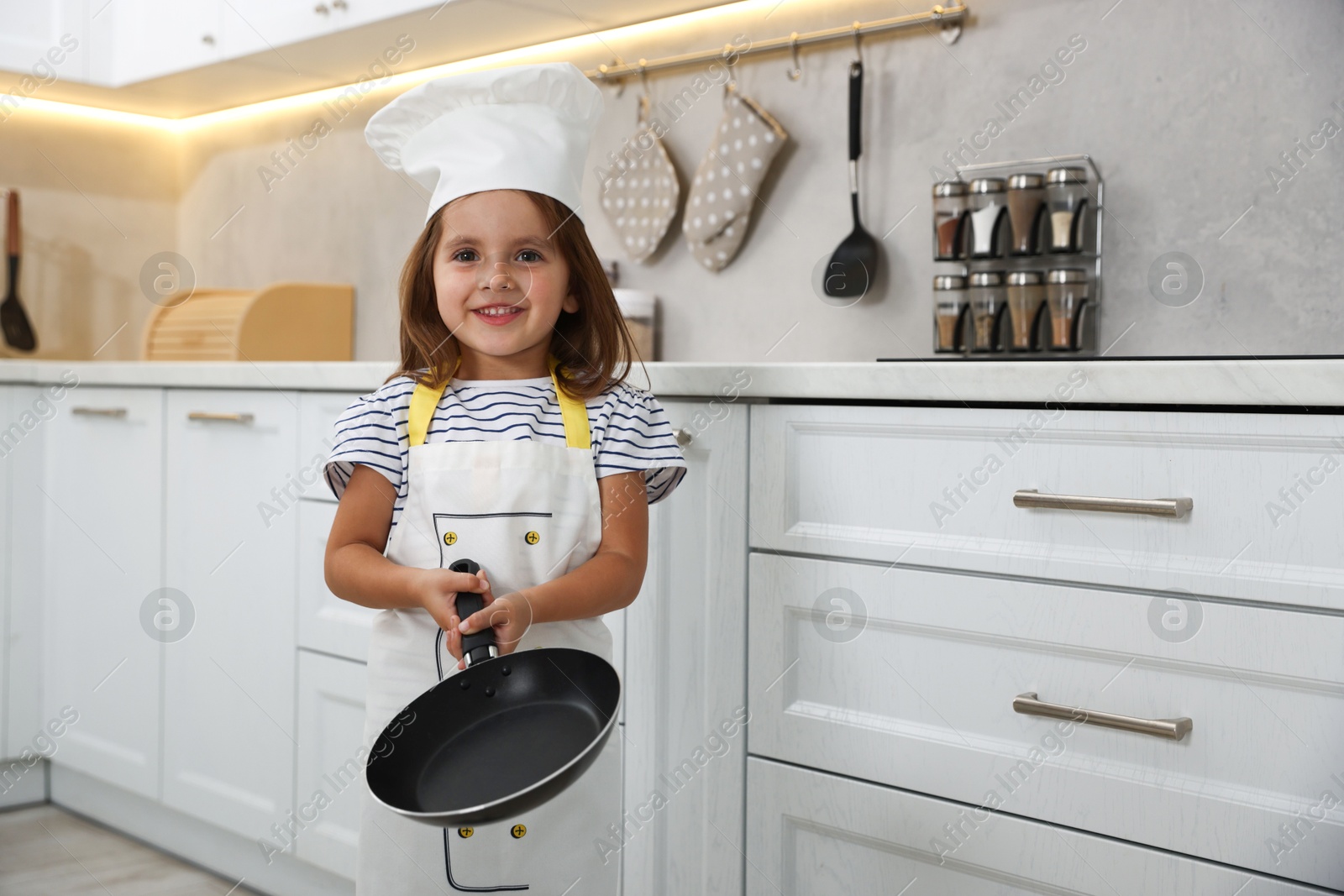 Photo of Choice of profession. Little girl with frying pan pretending to be chef in kitchen