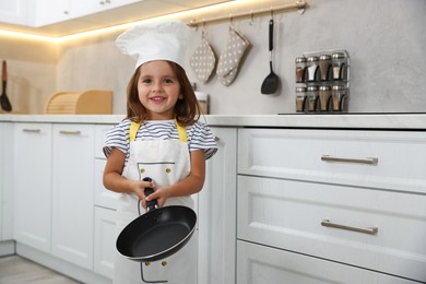 Photo of Choice of profession. Little girl with frying pan pretending to be chef in kitchen