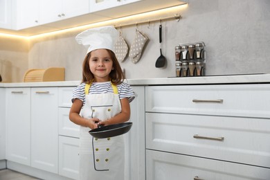 Photo of Choice of profession. Little girl with frying pan pretending to be chef in kitchen