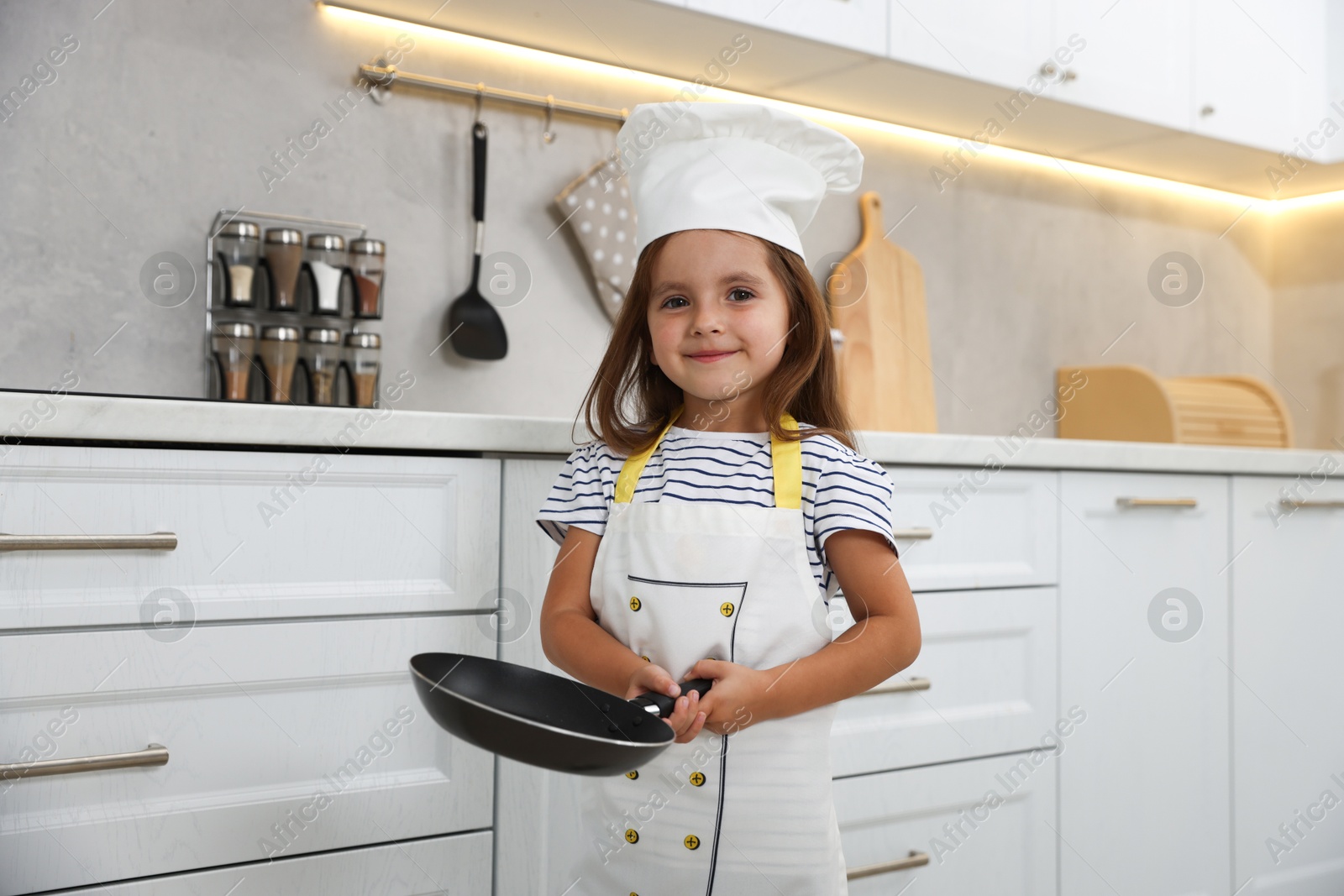 Photo of Choice of profession. Little girl with frying pan pretending to be chef in kitchen